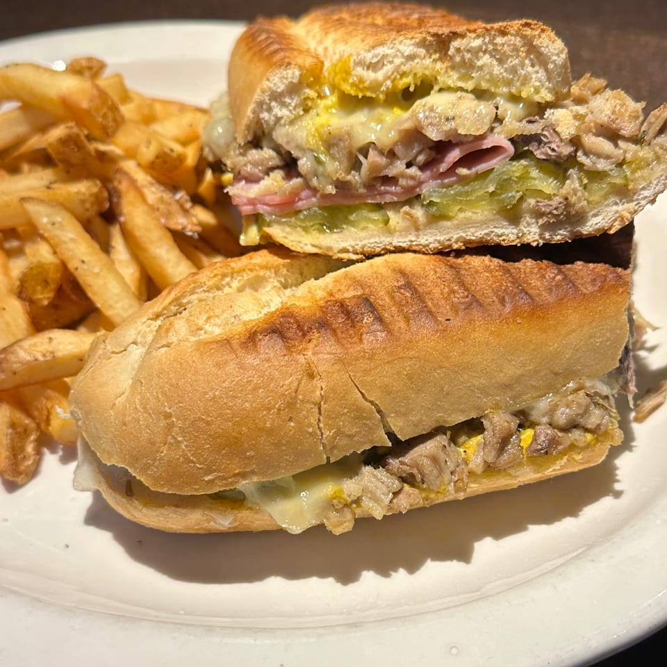 A Cuban sandwich, cut in half, with fries on a white plate at Johnny Gringo Painesville.