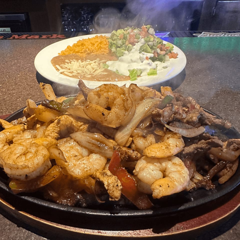 Sizzling shrimp and steak fajitas with onions and peppers, served with rice, beans, and guacamole.