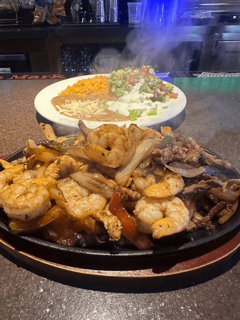 Sizzling shrimp and steak fajitas with onions and peppers, served with rice, beans, and guacamole.